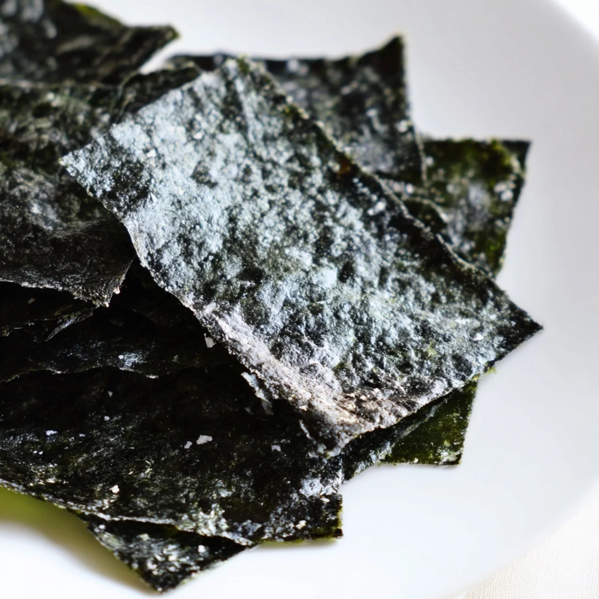 Golden roasted seaweed chips on a baking sheet, crispy and dark green, lightly brushed with sesame oil and sprinkled with sea salt.  
