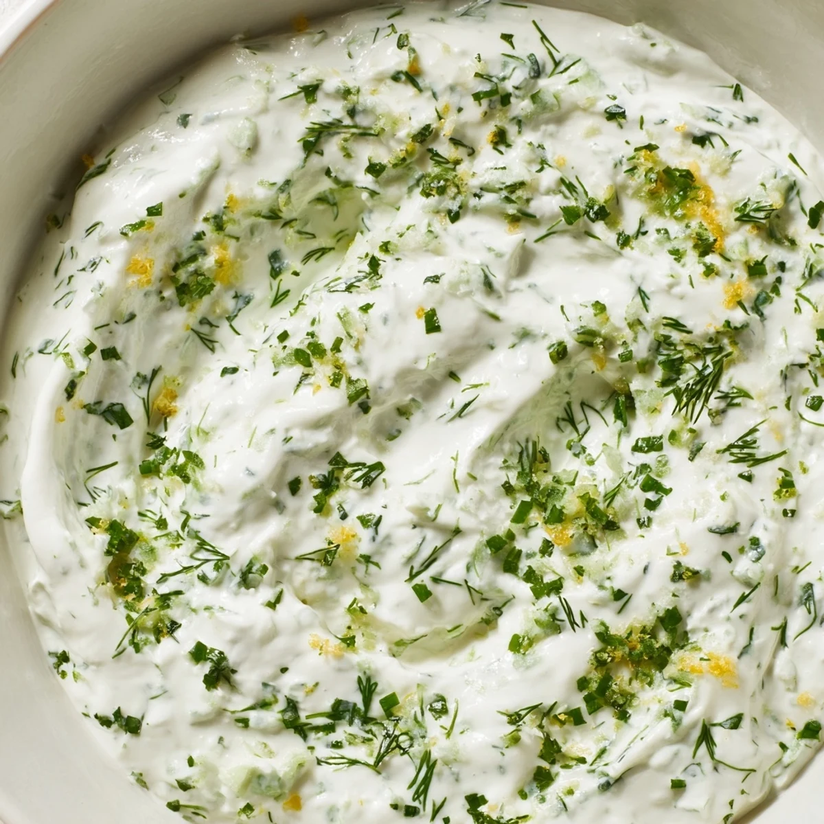 A close-up of creamy Greek Yogurt Herb Dip, showcasing the bright flecks of fresh dill, chives, and parsley.