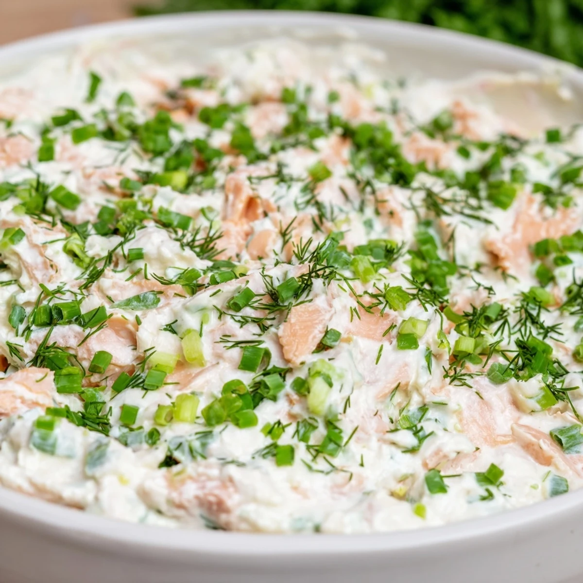 Smooth, rich smoked salmon dip in a white bowl, topped with lemon zest and fresh herbs for an elegant appetizer.