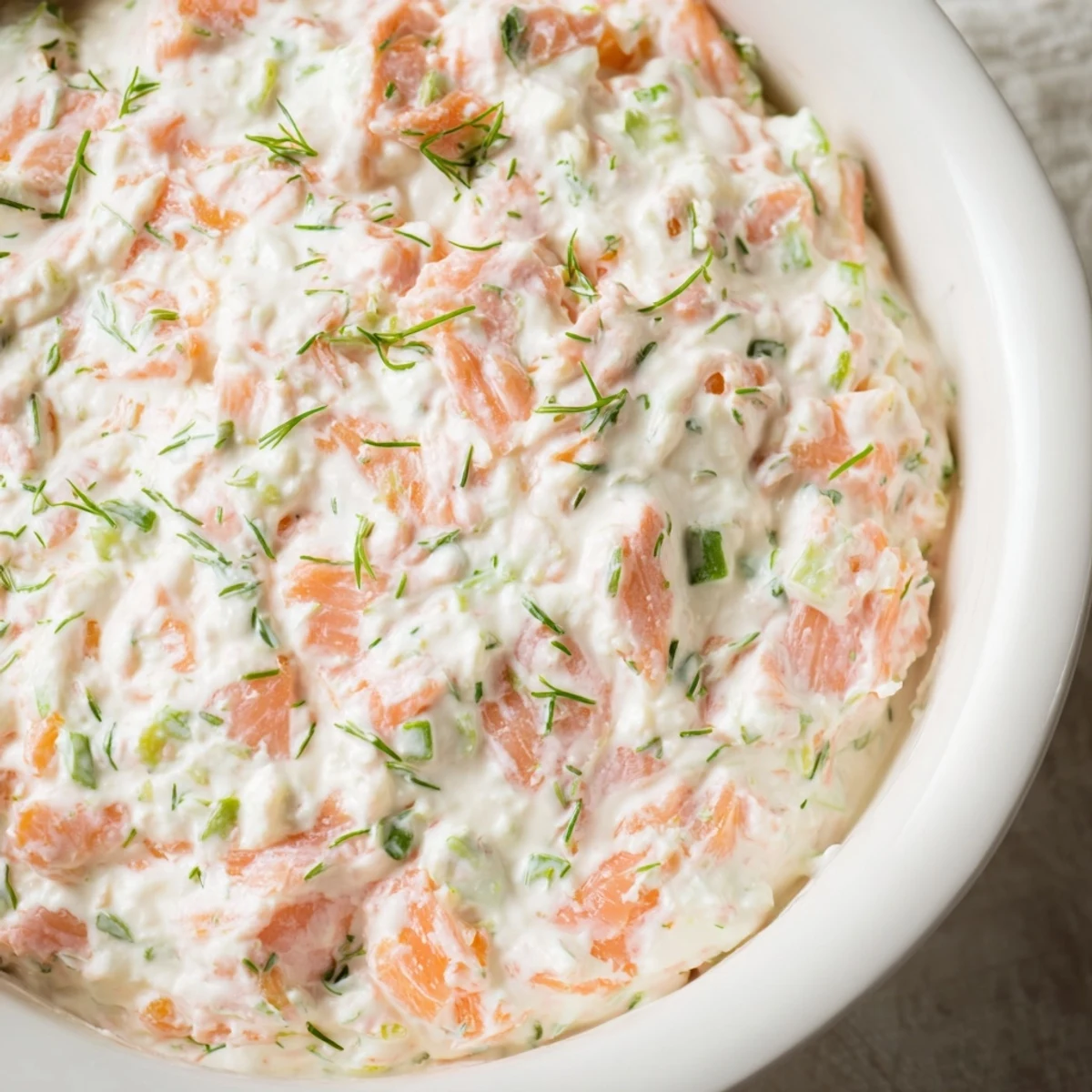 Freshly prepared smoked salmon dip with visible flakes of fish and herbs, paired with rye bread and lemon wedges.