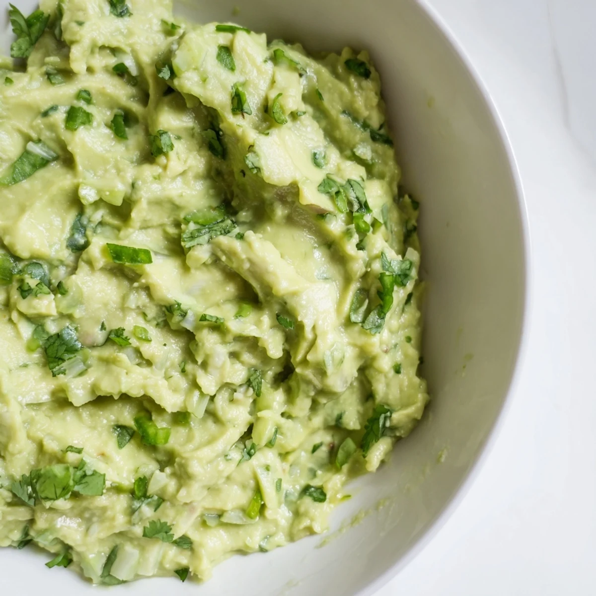 Homemade avocado lime dip with bright green color, lime wedges, and cilantro, ready for dipping with crunchy chips.