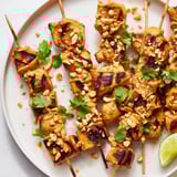Juicy Spicy Peanut Satay Chicken Skewers, served with fresh cilantro and lime wedges for a flavorful meal.