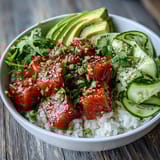A close-up of an Avocado Salmon Bowl topped with chopped peanuts, cucumber slices, and a dollop of wasabi for an umami kick.