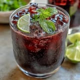 Glistening purple Black Currant Mocktail in a tall glass, packed with ice and fresh mint sprigs for a summer sip.