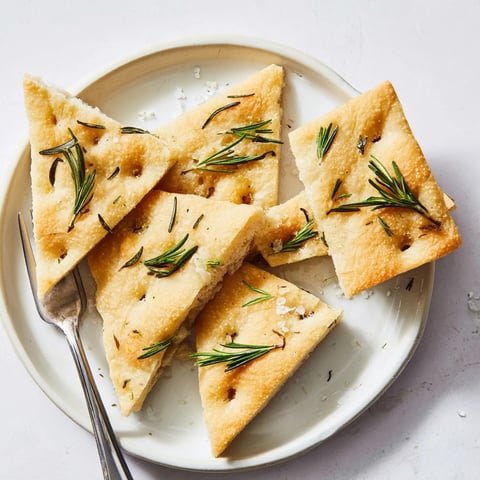Golden, crisp holiday bread focaccia, studded with rosemary; ready to serve on a plate.