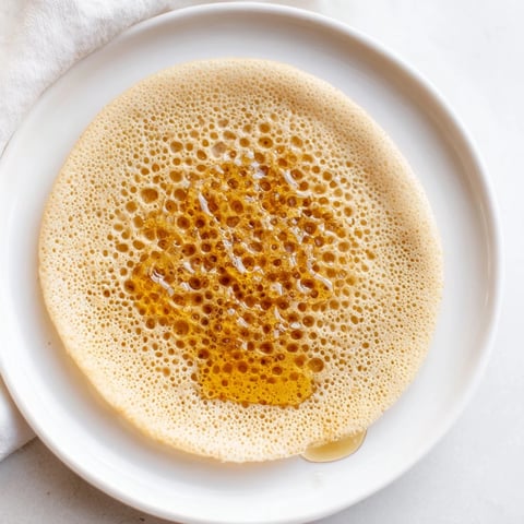 Golden Moroccan Baghrir crepes are bubbling, ready to soak up rich butter and sweet honey.