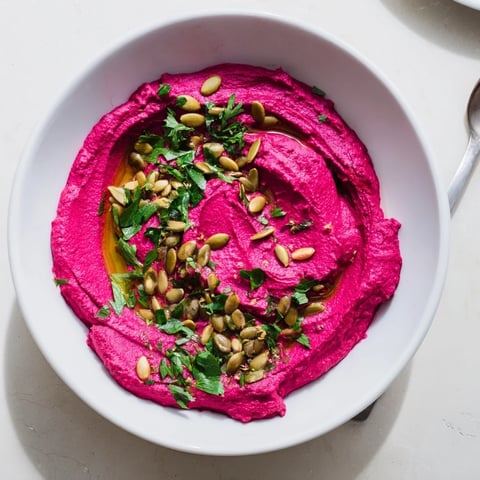 Vibrant beet hummus in a rustic bowl, garnished with olive oil and toasted pumpkin seeds.