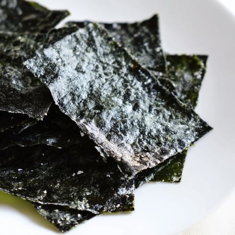 Golden roasted seaweed chips on a baking sheet, crispy and dark green, lightly brushed with sesame oil and sprinkled with sea salt.  