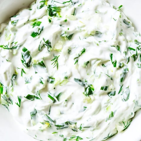 A vibrant bowl of Greek Yogurt Herb Dip, surrounded by colorful fresh vegetable crudités and pita chips for dipping.