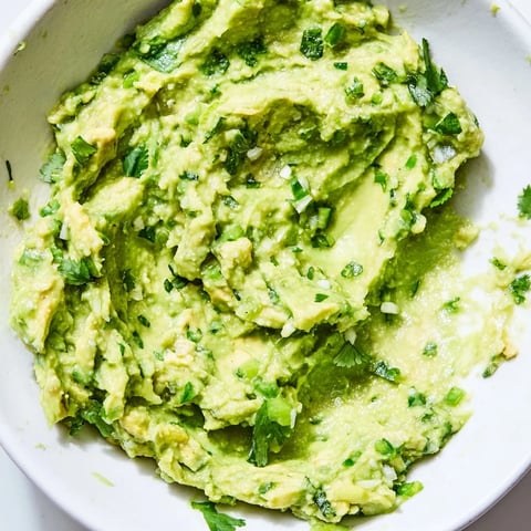 Creamy avocado lime dip garnished with cilantro, served with tortilla chips and fresh vegetable sticks on a rustic table.