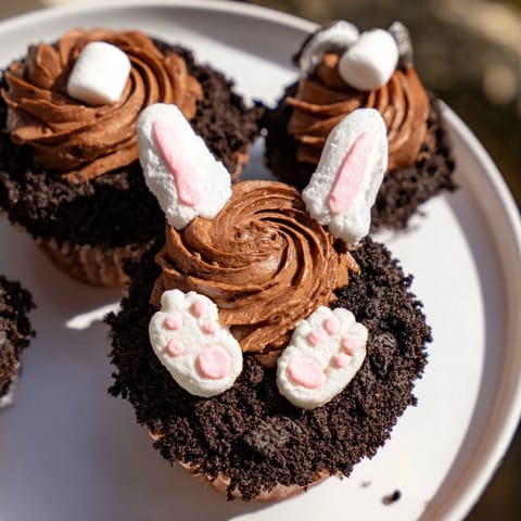 Chocolate buttercream frosts these Bunny Burrow Cupcake Tray cupcakes, featuring a chocolate cookie "soil" and playful bunny details.