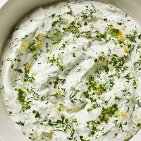 A close-up of creamy Greek Yogurt Herb Dip, showcasing the bright flecks of fresh dill, chives, and parsley.