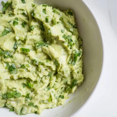 Homemade avocado lime dip with bright green color, lime wedges, and cilantro, ready for dipping with crunchy chips.