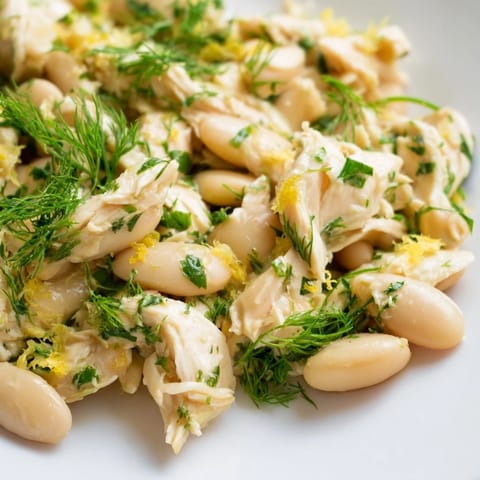 Overhead view of Lemony White Bean Chicken Salad served on a rustic wooden table, featuring vibrant red cherry tomatoes and bright green parsley for a fresh, summer-inspired look.  