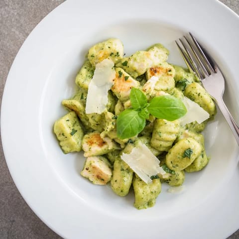Creamy pesto gnocchi with chicken served in a white bowl, garnished with fresh basil and extra Parmesan.