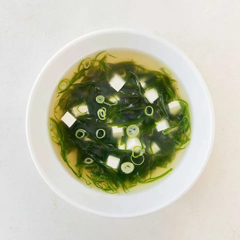 A spoon dips into savory wakame soup, revealing tender tofu and vibrant green seaweed in a fragrant, mineral-rich dashi broth.  