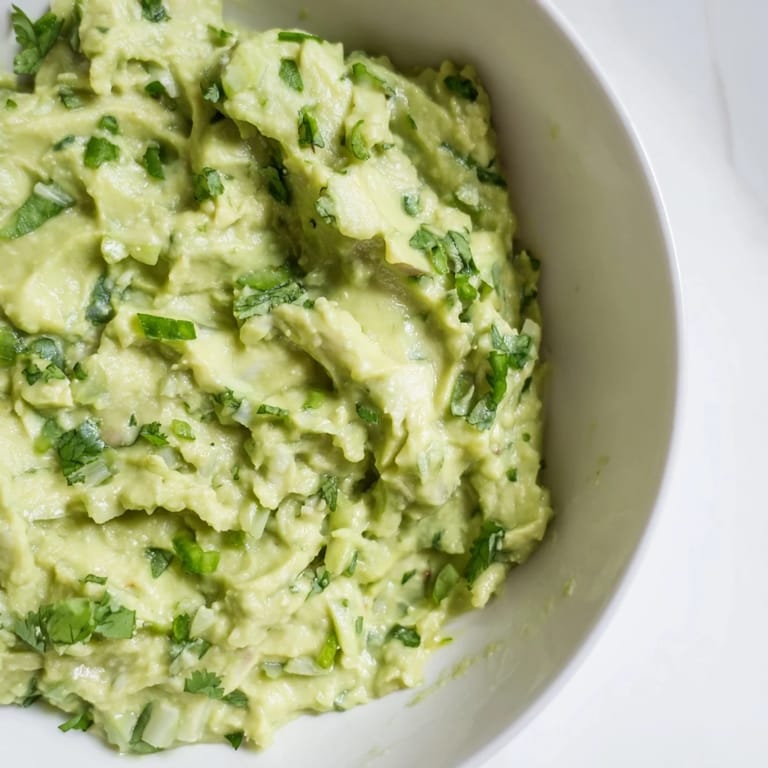 Homemade avocado lime dip with bright green color, lime wedges, and cilantro, ready for dipping with crunchy chips.