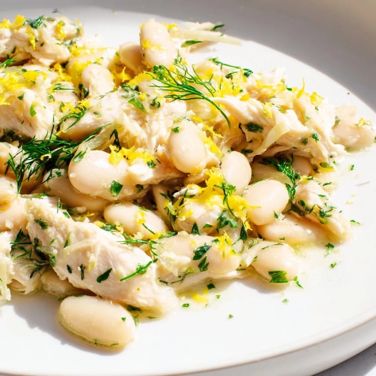 A serving fork lifts a generous portion of Lemony White Bean Chicken Salad, revealing the protein-rich mix of chicken and white beans tossed in a zesty lemon dressing.