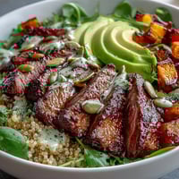 Golden roasted butternut squash steak bowls are topped with creamy avocado, sliced steak, and vibrant greens on fluffy quinoa.