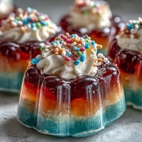 Rainbow Jello Cups for Kids: Bright, colorful layers of fruity gelatin stacked in clear cups, topped with fluffy whipped cream and rainbow sprinkles.